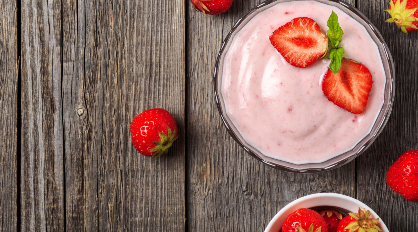 Frischer Erdbeerjoghurt mit ganzen Erdbeeren auf rustikalem Holztisch als Beispiel für gekühlte Lebensmittel und Desserts.