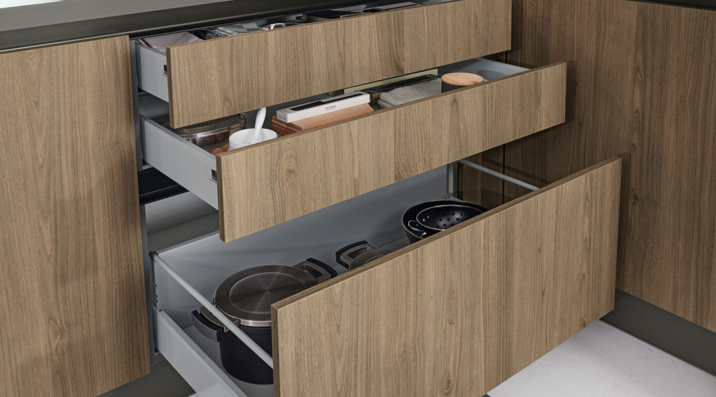 Geöffnete Küchenschubladen mit Holzfronten und übersichtlichem Stauraum für Töpfe, Pfannen und Küchenutensilien in einer modernen Einbauküche.