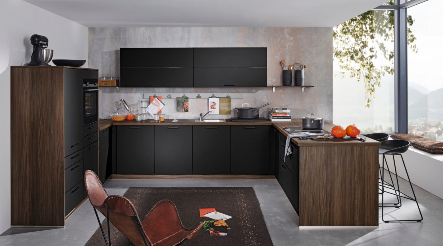 Moderne schwarze Wohnküche mit Holzfronten, Holzarbeitsplatte, Kücheninsel, Barhockern und Teppich vor großer Fensterfront – wohnlich und klar gestaltet.