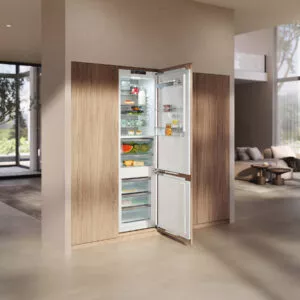 Integrierter Miele Einbaukühlschrank mit offener Tür und übersichtlich angeordneten Lebensmitteln, eingebettet in eine moderne Küchenfront in Holzoptik