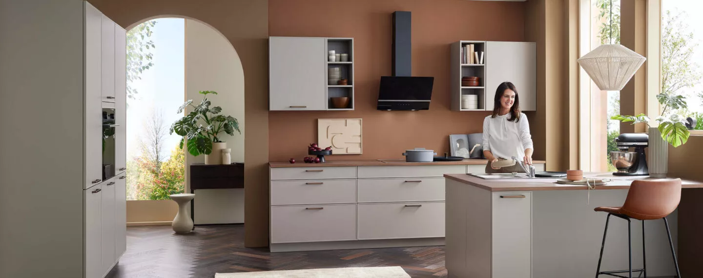 Moderne Bauformat Küche in warmen Beige- und Erdtönen mit Kochinsel, offenen Regalen und integriertem Essbereich – präsentiert bei Küchen Concept in Heßdorf