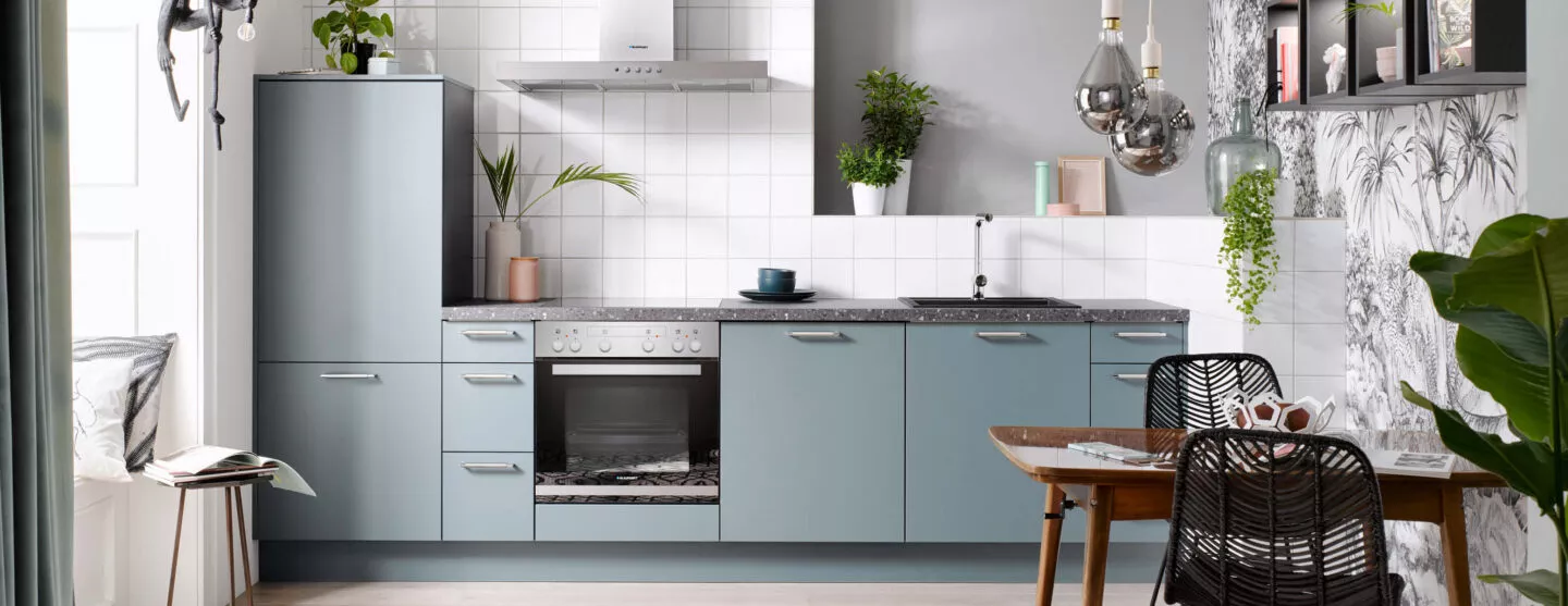 Klassische Pantryküche in Blau mit Arbeitsplatte in Steinoptik, Herd, Backofen und Spüle, kombiniert mit offenen Regalen und Pflanzen für wohnliche Atmosphäre.