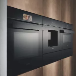 „Moderne Siemens Einbau-Dampfgarer und Backöfen mit schwarzer Glasfront und Touchdisplay, integriert in eine hochwertige Küchenwand in Holzoptik