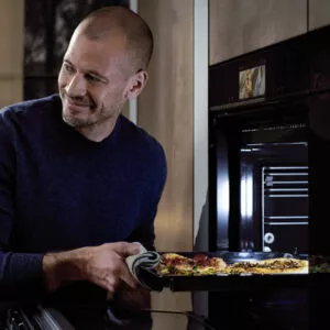 Mann nimmt ein frisch gebackenes Gericht aus einem modernen Einbau-Backofen mit Touchdisplay in einer stilvollen Küche