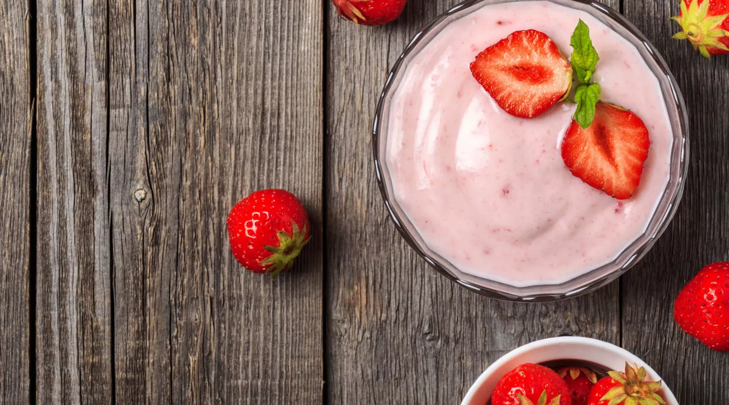 Frischer Erdbeerjoghurt mit ganzen Erdbeeren auf rustikalem Holztisch als Beispiel für gekühlte Lebensmittel und Desserts.