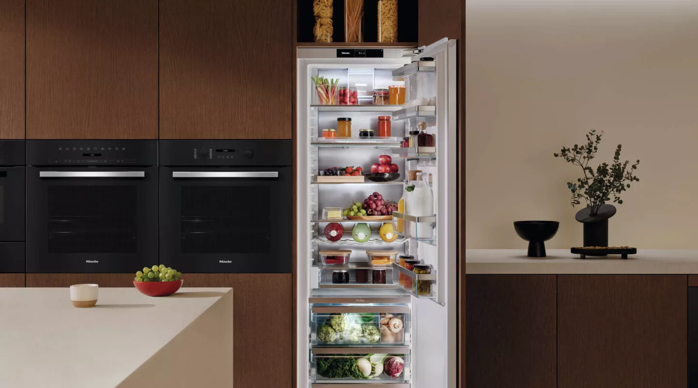 Mann vor geöffnetem Kühlschrank mit frischen Lebensmitteln und Torte, zeigt großzügigen Stauraum und moderne Kühltechnologie.