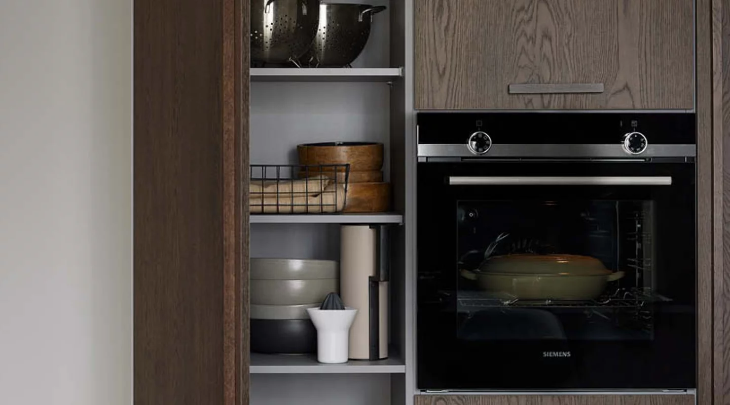 Moderner Siemens-Einbaubackofen in einem Küchenhochschrank mit Holzfronten, daneben offene Regalfächer mit Geschirr und Küchenutensilien – funktionale Küchenmöbel für eine moderne Einbauküche.