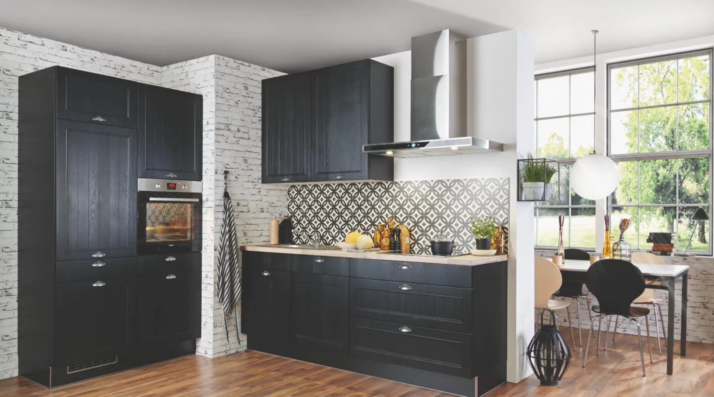 Moderne Landhausküche mit dunklen Rahmenfronten, heller Arbeitsplatte, gemusterter Küchenrückwand, Einbaubackofen und Edelstahl-Dunstabzugshaube, kombiniert mit offenem Essbereich, großen Fenstern und Holzboden.